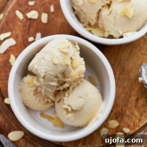 Close-up of creamy almond milk ice cream scooped into a white ramekin, topped with sliced almonds, sitting on a wooden board.