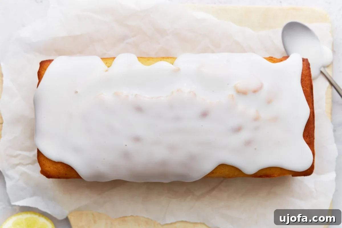 Iced lemon loaf on parchment paper with glaze spread evenly over the top.