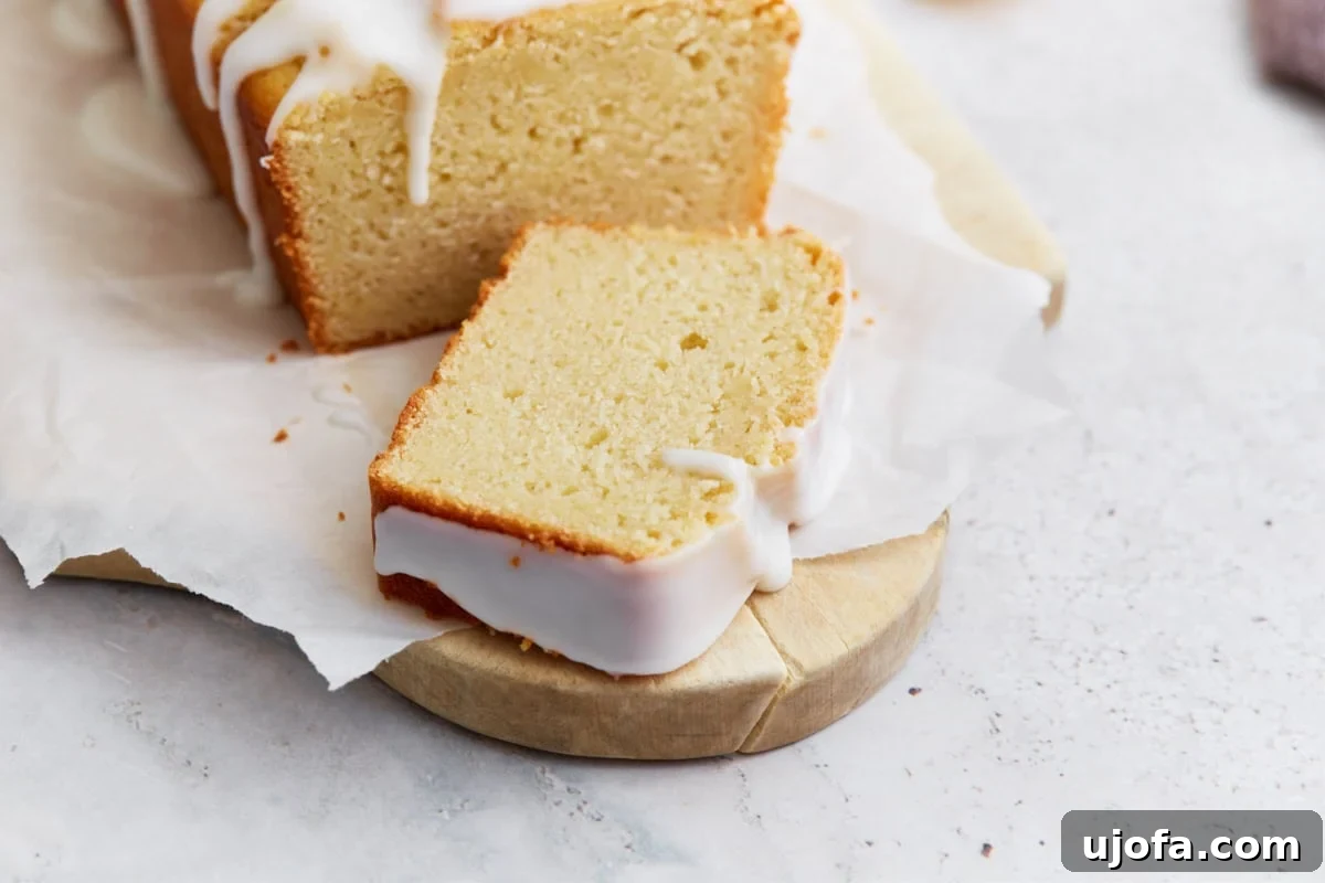 A single slice of gluten-free iced lemon loaf laid flat on parchment, showing the moist crumb and thick glaze along the edges.