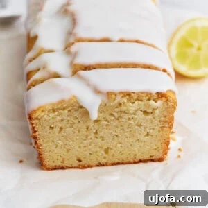 Sliced gluten-free iced lemon loaf on parchment paper with a thick white glaze dripping over the edges.