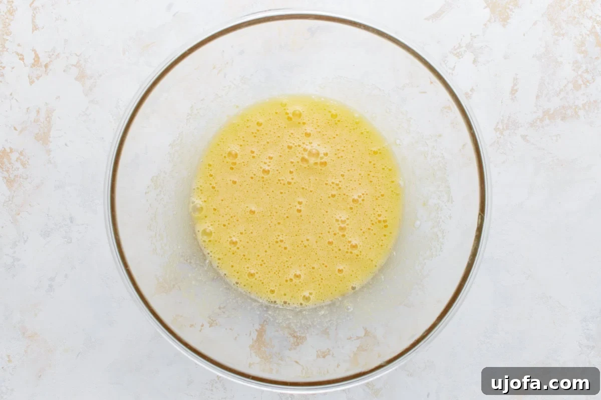 Whisked eggs and sugar in a clear glass bowl, lightly frothy and pale yellow.
