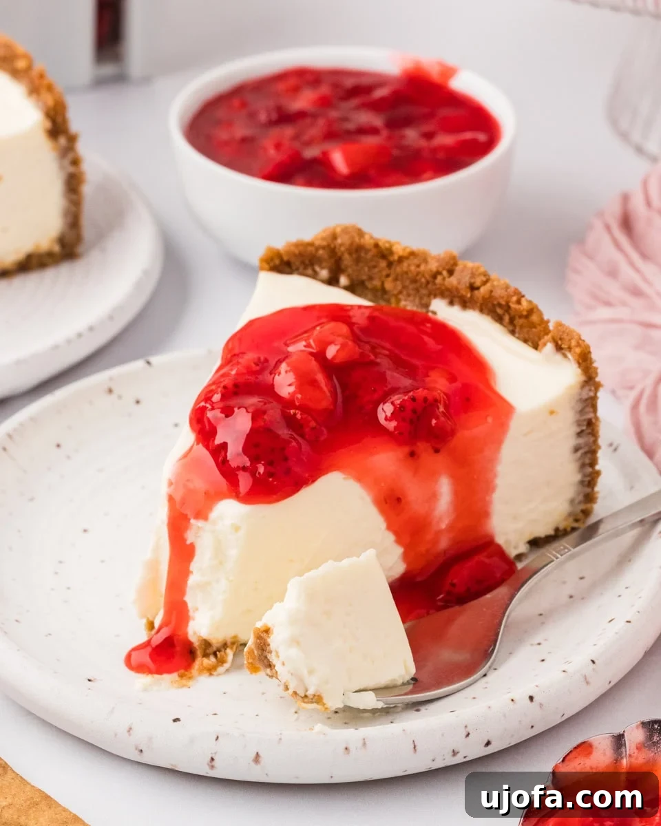 No-Oven Gluten-Free Cheesecake Bliss 2 A perfectly sliced gluten-free no-bake cheesecake, generously topped with vibrant strawberry sauce, rests on a speckled plate. A spoonful has been taken, revealing its creamy texture, with a silver spoon placed elegantly beside it.