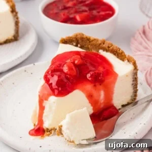 A slice of gluten-free no-bake cheesecake topped with strawberry sauce on a speckled plate, with a bite taken and a spoon beside it.