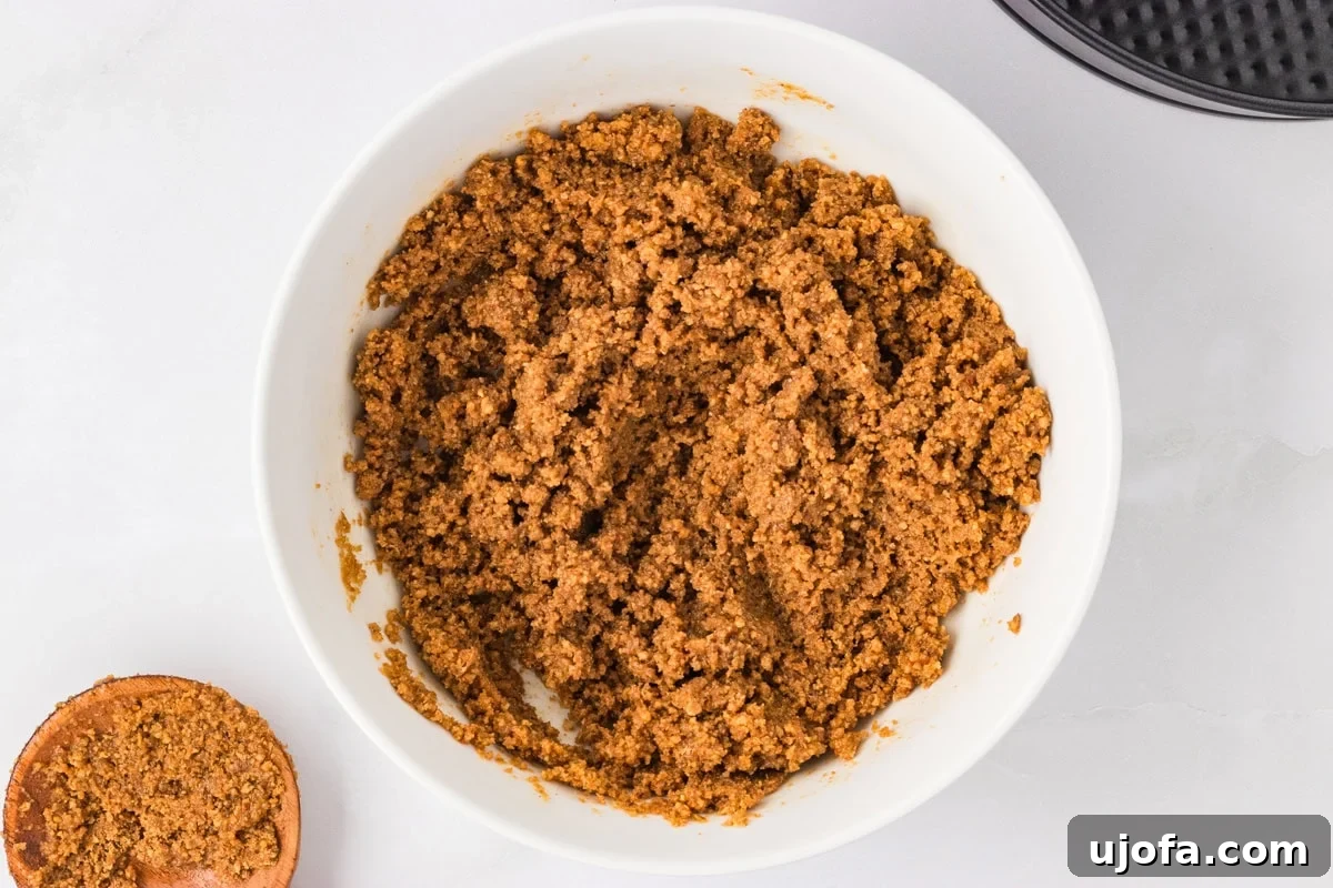 No-Oven Gluten-Free Cheesecake Bliss 5 A white mixing bowl contains a perfectly blended mixture of gluten-free graham cracker crumbs, brown sugar, cinnamon, and melted butter, forming the base for the cheesecake crust.