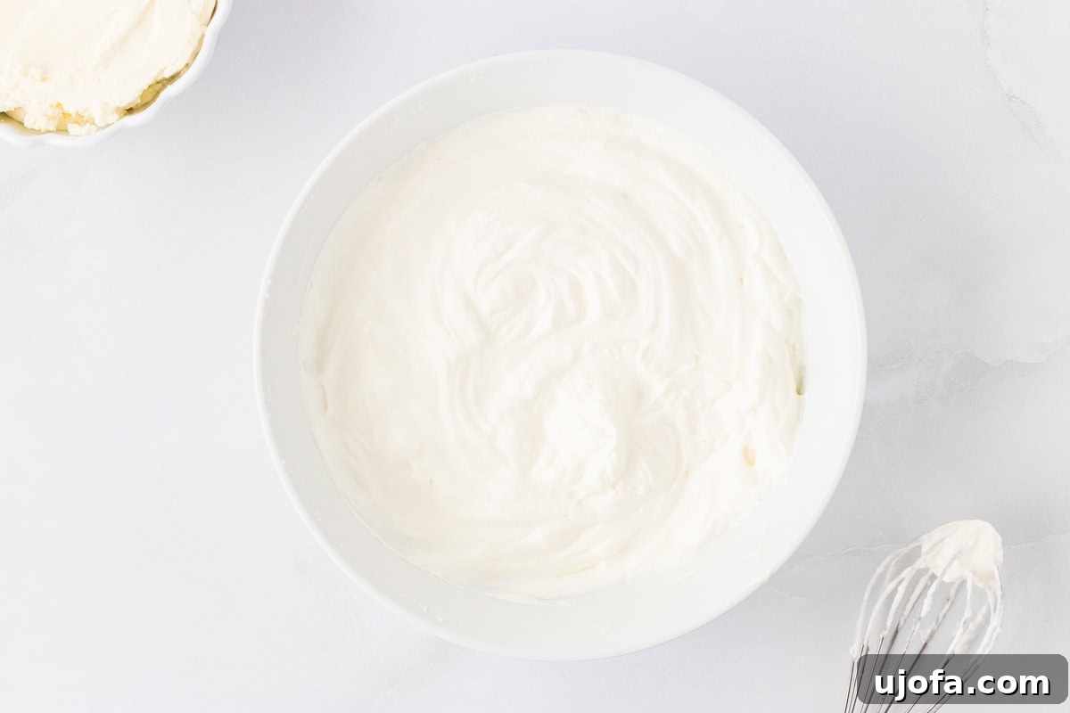 No-Oven Gluten-Free Cheesecake Bliss 8 A bowl filled with light, airy, and fluffy whipped cream, showing distinct stiff peaks formed by whipping cold heavy cream with a hand mixer.