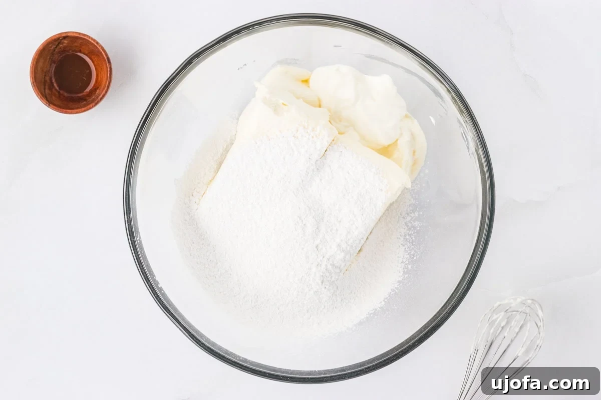 No-Oven Gluten-Free Cheesecake Bliss 9 A large mixing bowl containing softened cream cheese, sour cream, and powdered sugar, with a whisk attachment poised above, ready to be blended into a smooth and creamy cheesecake base.