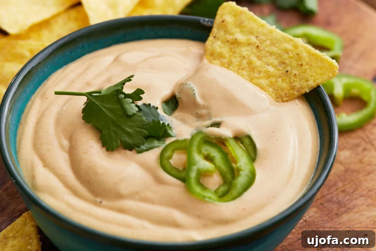 Creamy Cashew Queso 8 Close-up shot of a crunchy tortilla chip generously scooped with creamy cashew queso dip, showcasing the rich texture and delicious toppings.