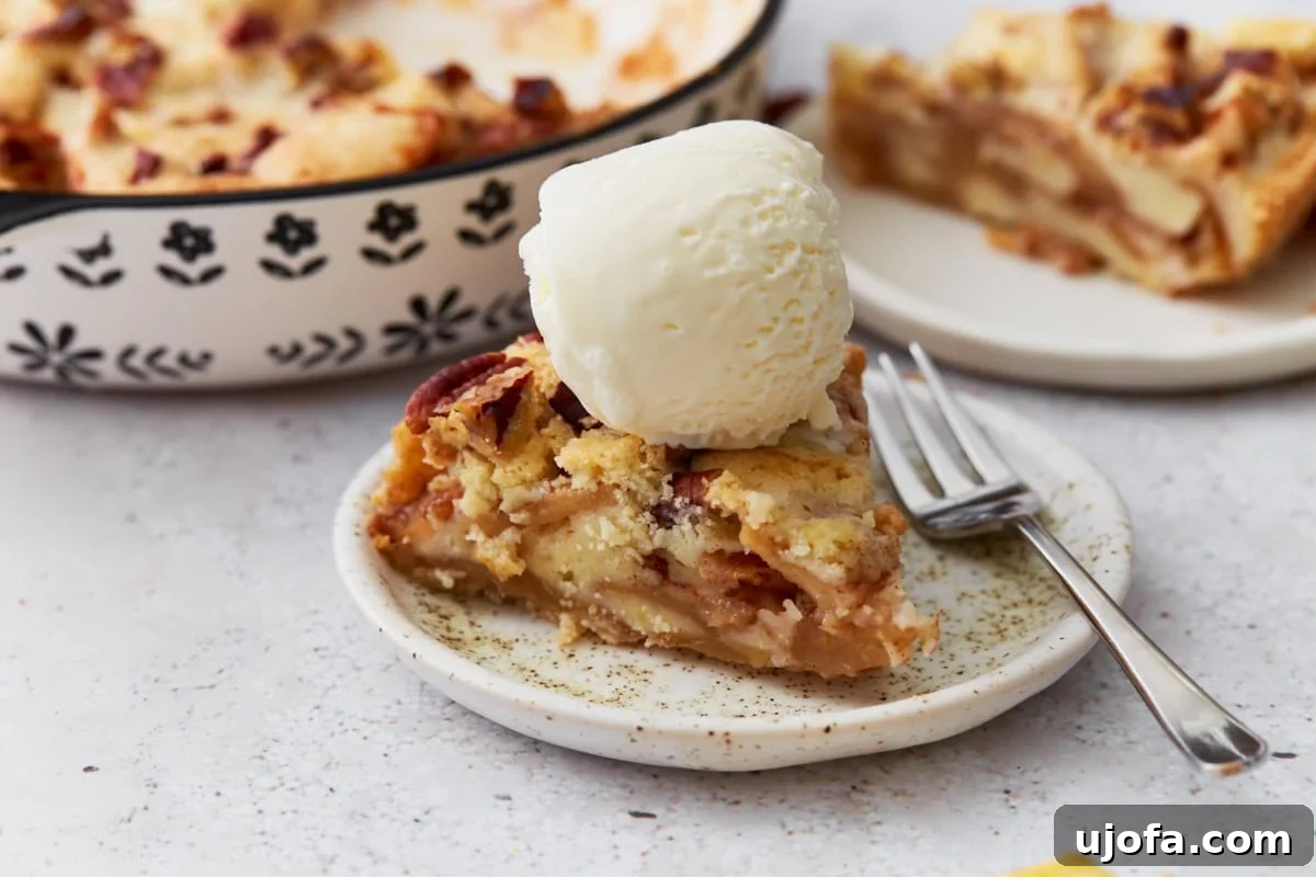 Easy Crustless Apple Pie 11 Slice of crustless apple pie topped with a scoop of vanilla ice cream on a small plate with a fork, with the full pie in the background.
