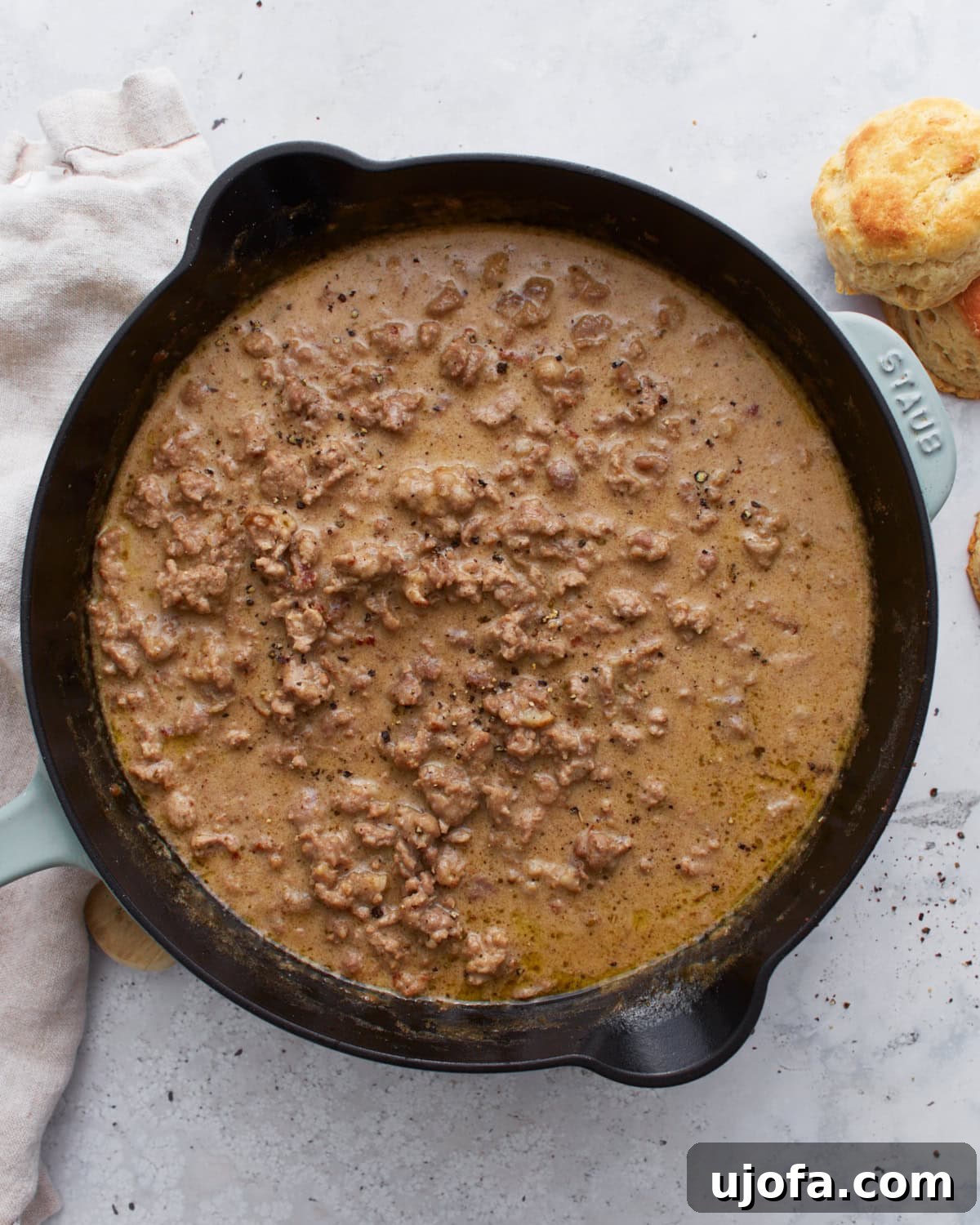 Creamy Gluten-Free Sausage Gravy 2 Overhead view of a cast iron skillet filled with thick, creamy gluten-free sausage gravy, with golden biscuits on the side, ready to be served.