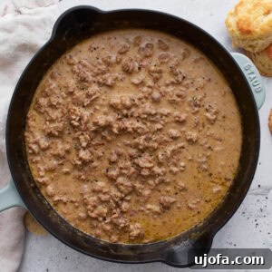 Overhead view of a cast iron skillet filled with thick, creamy gluten-free sausage gravy, with golden biscuits on the side.