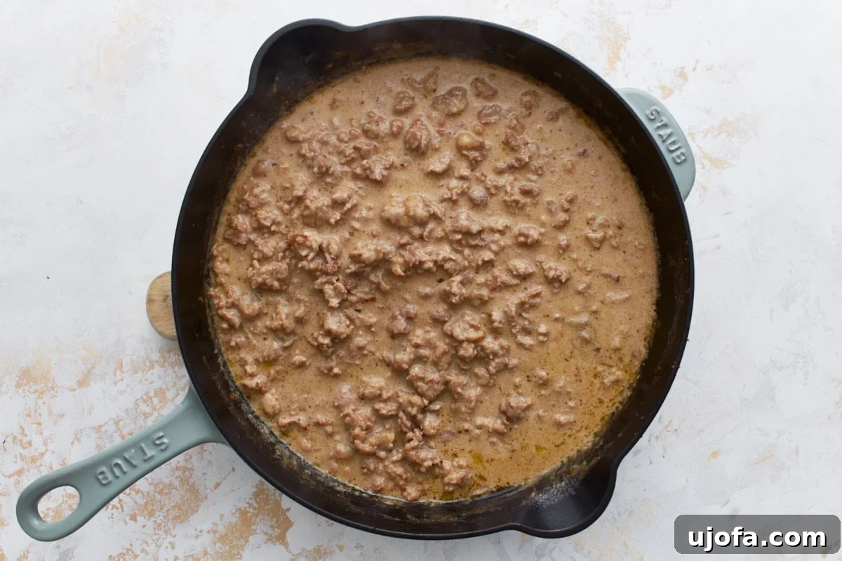 Creamy Gluten-Free Sausage Gravy 7 Gluten-free sausage gravy simmering gently in a cast iron skillet, thickening beautifully as it cooks, with a rich, creamy texture beginning to form.