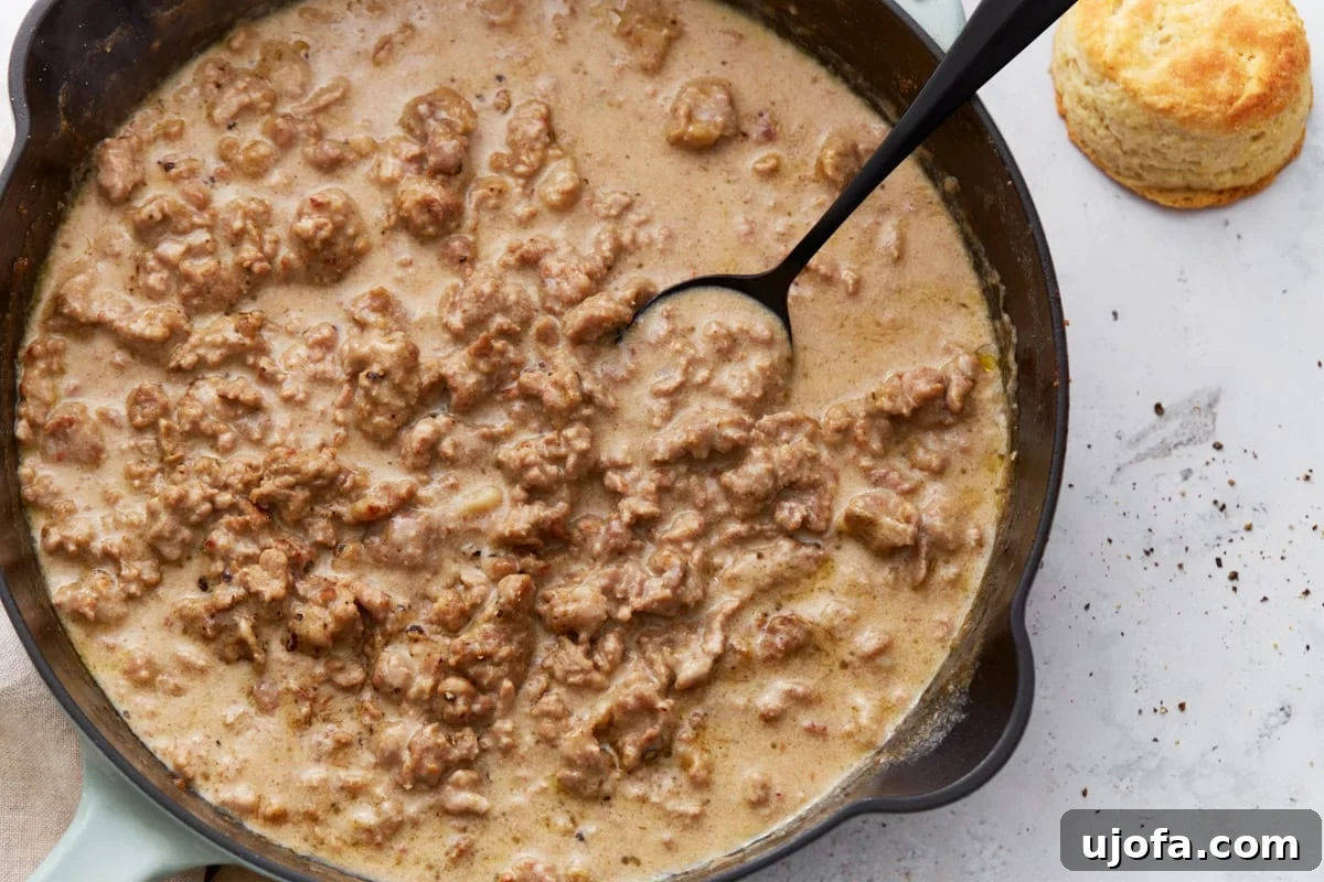 Creamy Gluten-Free Sausage Gravy 9 A spoon laden with thick, creamy gluten-free sausage gravy, freshly scooped from a cast iron skillet, highlighting its rich texture and tempting aroma, with a golden biscuit nearby.