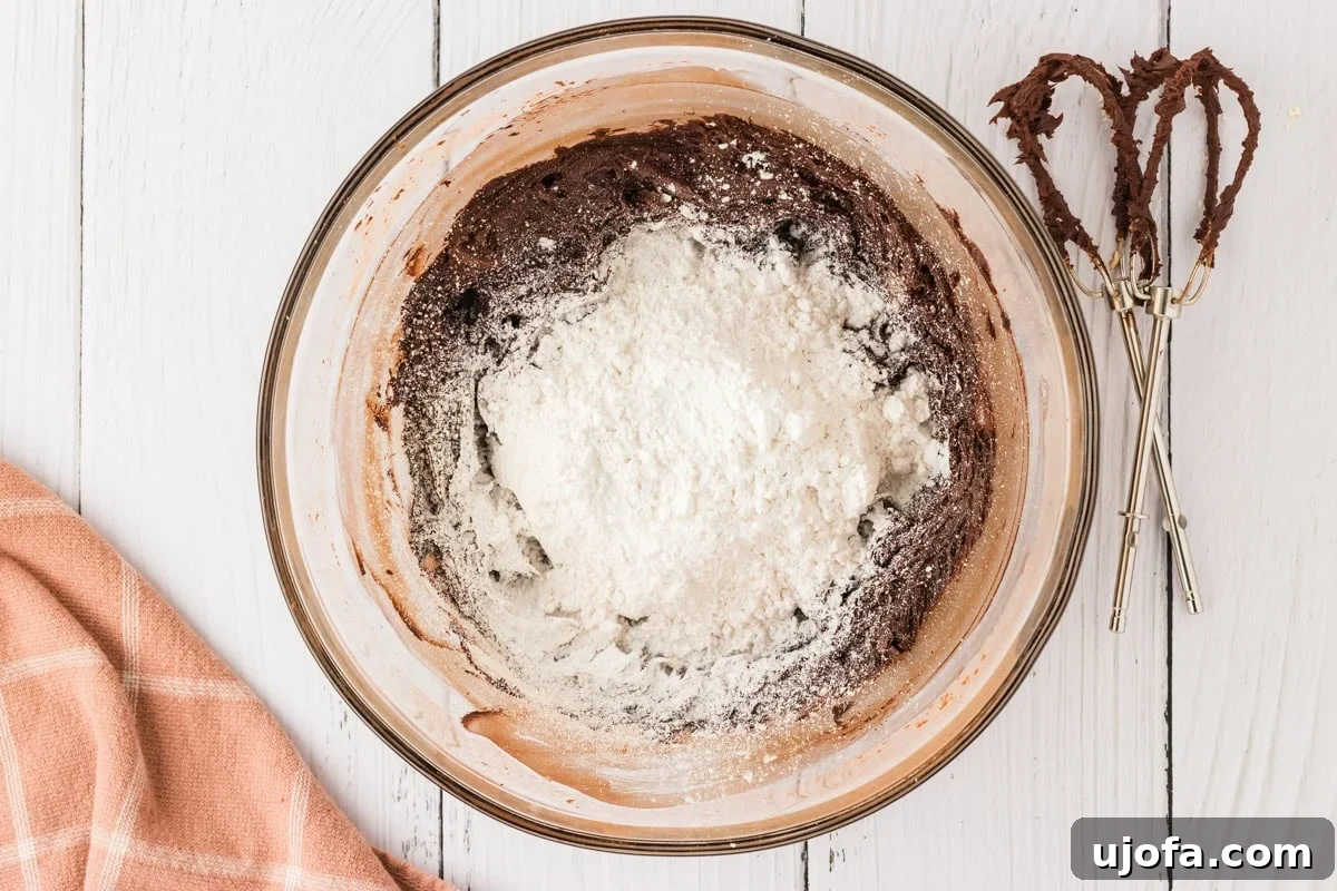 Effortless Gluten-Free Fudgy Cake 17 A glass bowl with chocolate frosting, with a mound of powdered sugar added on top, ready to be mixed.