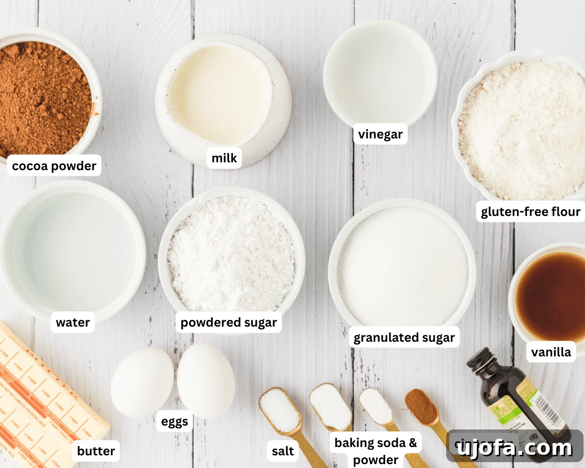 Effortless Gluten-Free Fudgy Cake 4 Assortment of gluten-free chocolate cake ingredients laid out on a white surface: milk, vinegar, gluten-free flour, baking powder, baking soda, salt, cinnamon, cocoa powder, butter, sugar, vanilla, eggs, and a cup of boiling water.