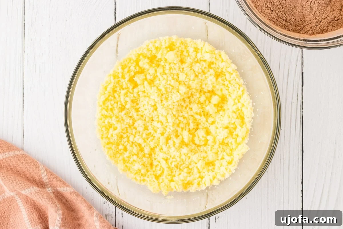 Effortless Gluten-Free Fudgy Cake 8 A glass mixing bowl with softened butter and sugar, creamed together, placed on a white wooden surface.