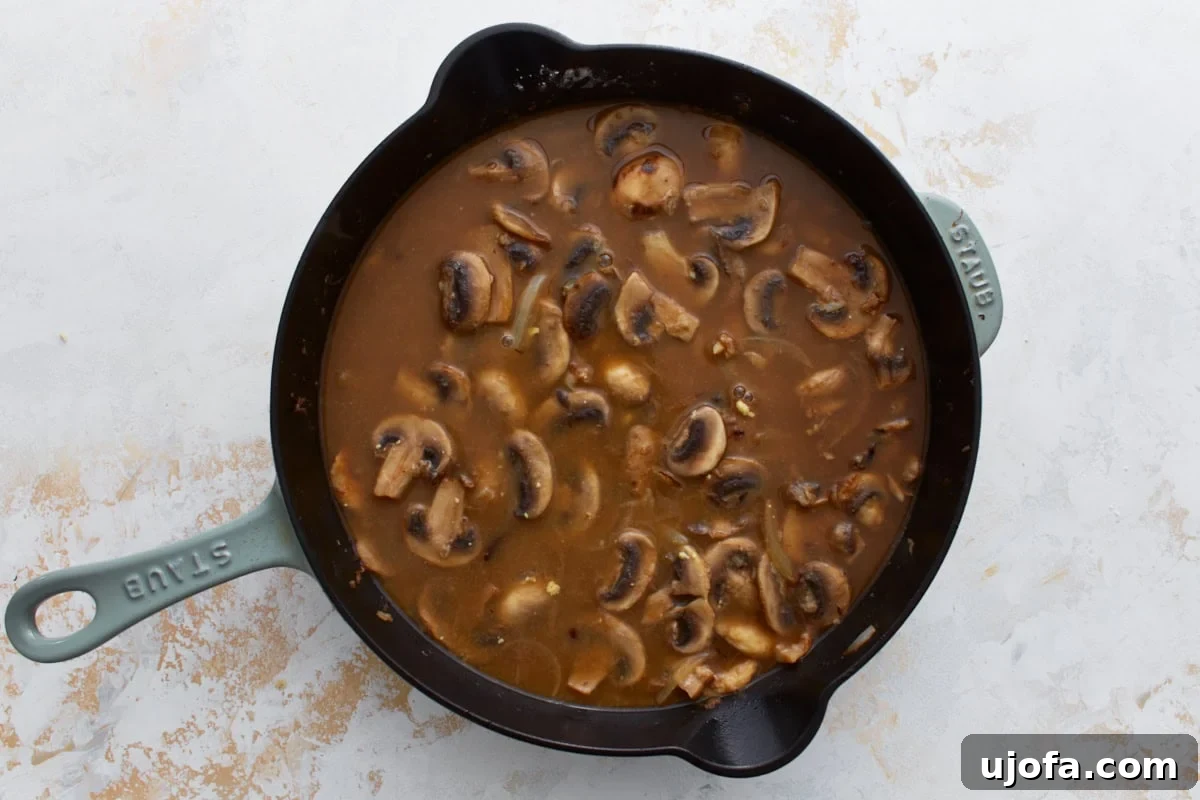 Beef broth added to the skillet, with mushrooms floating in the simmering sauce.