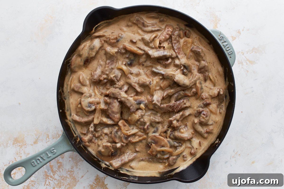 Overhead view of creamy gluten-free beef stroganoff in a black skillet, with visible slices of beef, mushrooms, and onions in a thick sauce.