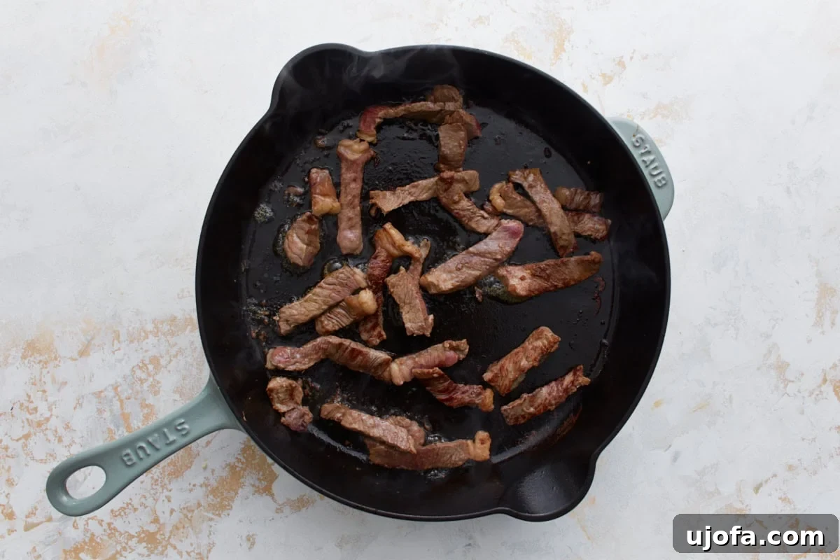 Beef strips searing in a hot cast iron skillet until browned.
