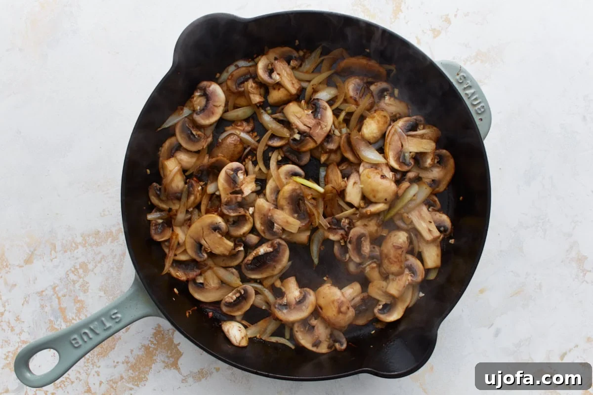 Mushrooms and onions cooking together in the skillet, releasing moisture and beginning to brown.