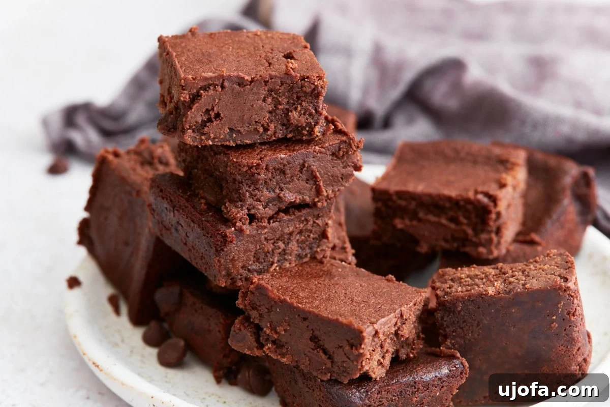 A plate of cut keto brownies stacked in a rustic pile, with rich chocolate color and soft interiors visible.