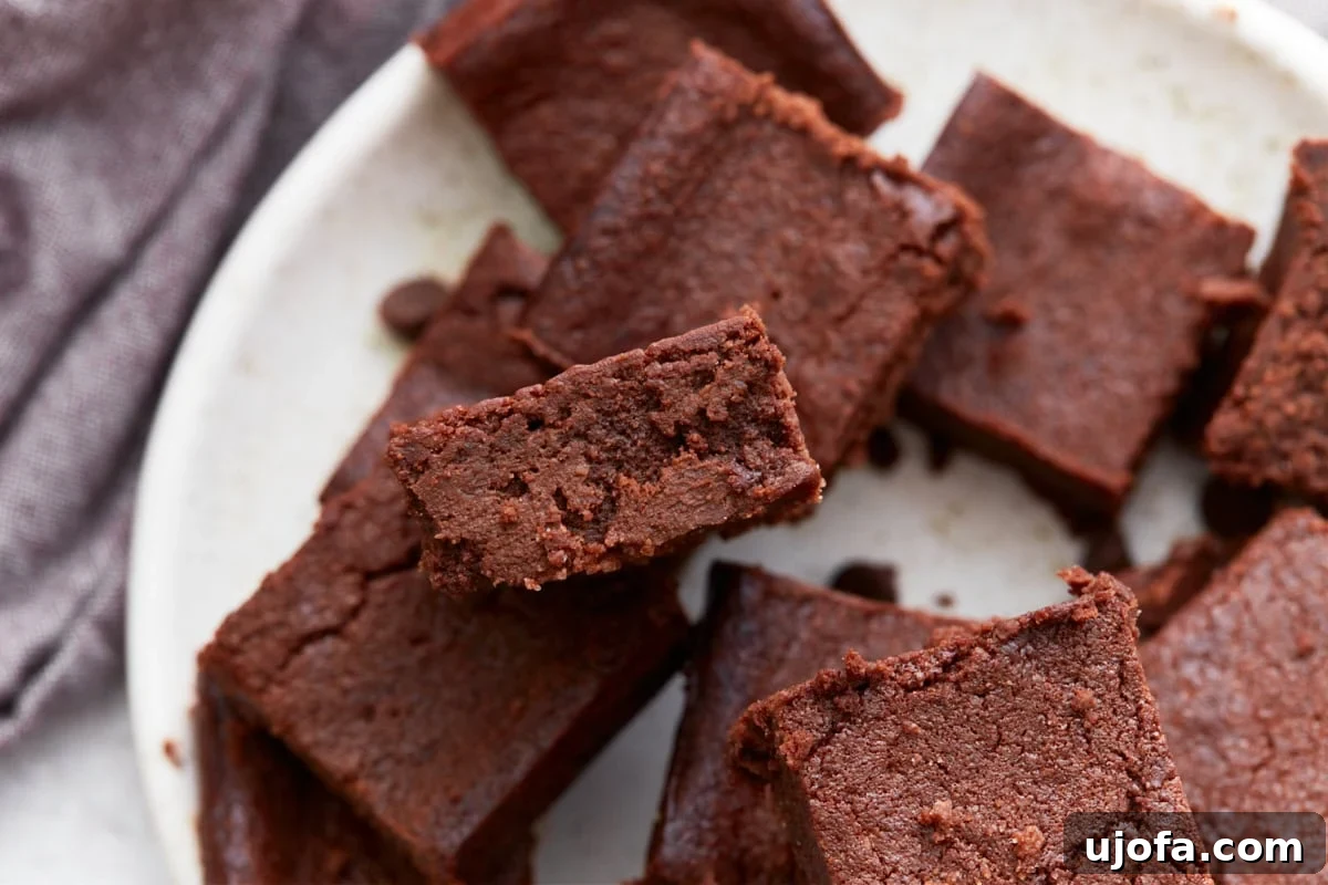 Overhead view of several keto brownies on a plate, with one brownie angled to show its moist, dense crumb.