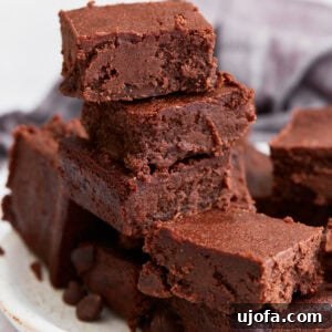 A stack of rich, fudgy keto brownies on a white plate, showing their dense, chocolatey texture with crispy edges.