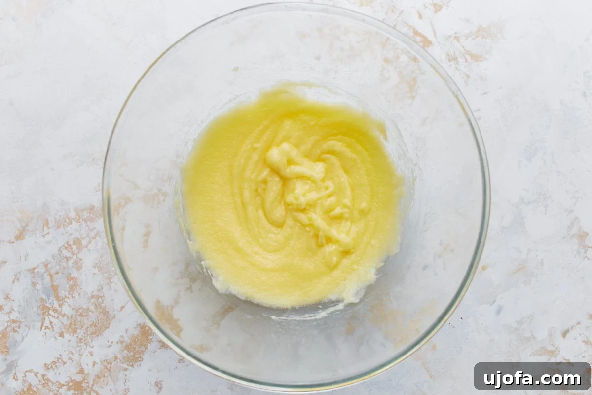 A glass bowl with melted butter and erythritol whisked together into a smooth yellow mixture.