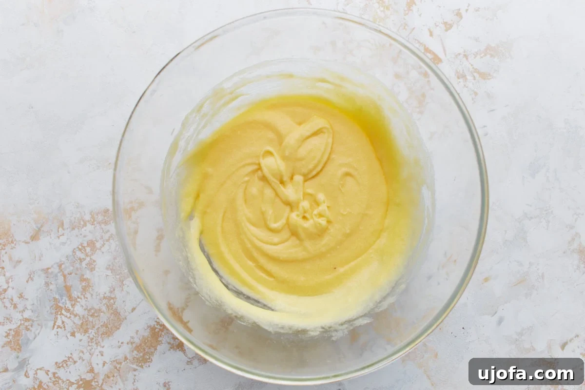 A glass bowl showing a creamy, pale yellow batter after eggs and vanilla have been added to the butter and sweetener mixture.