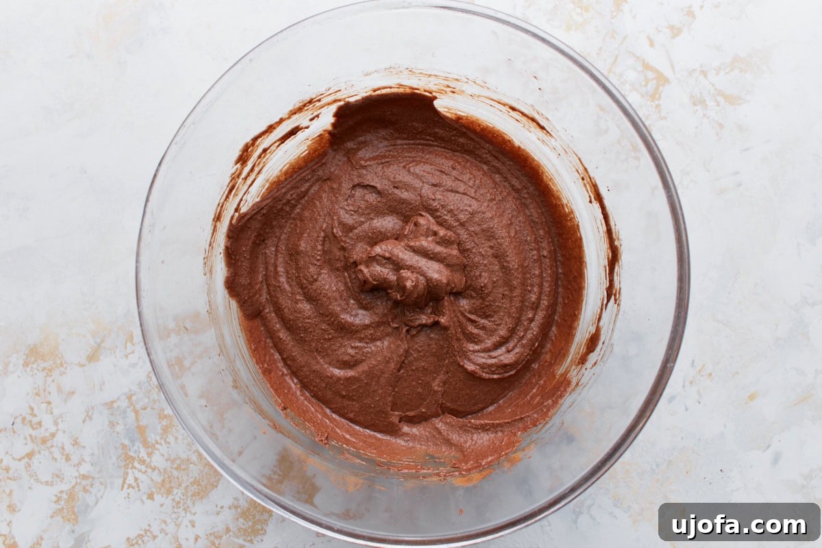 A glass bowl filled with thick chocolate brownie batter made with almond flour and cocoa powder.