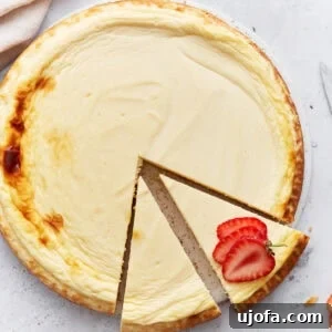 Whole baked keto cheesecake with one slice removed and garnished with fresh strawberry slices on a light background.