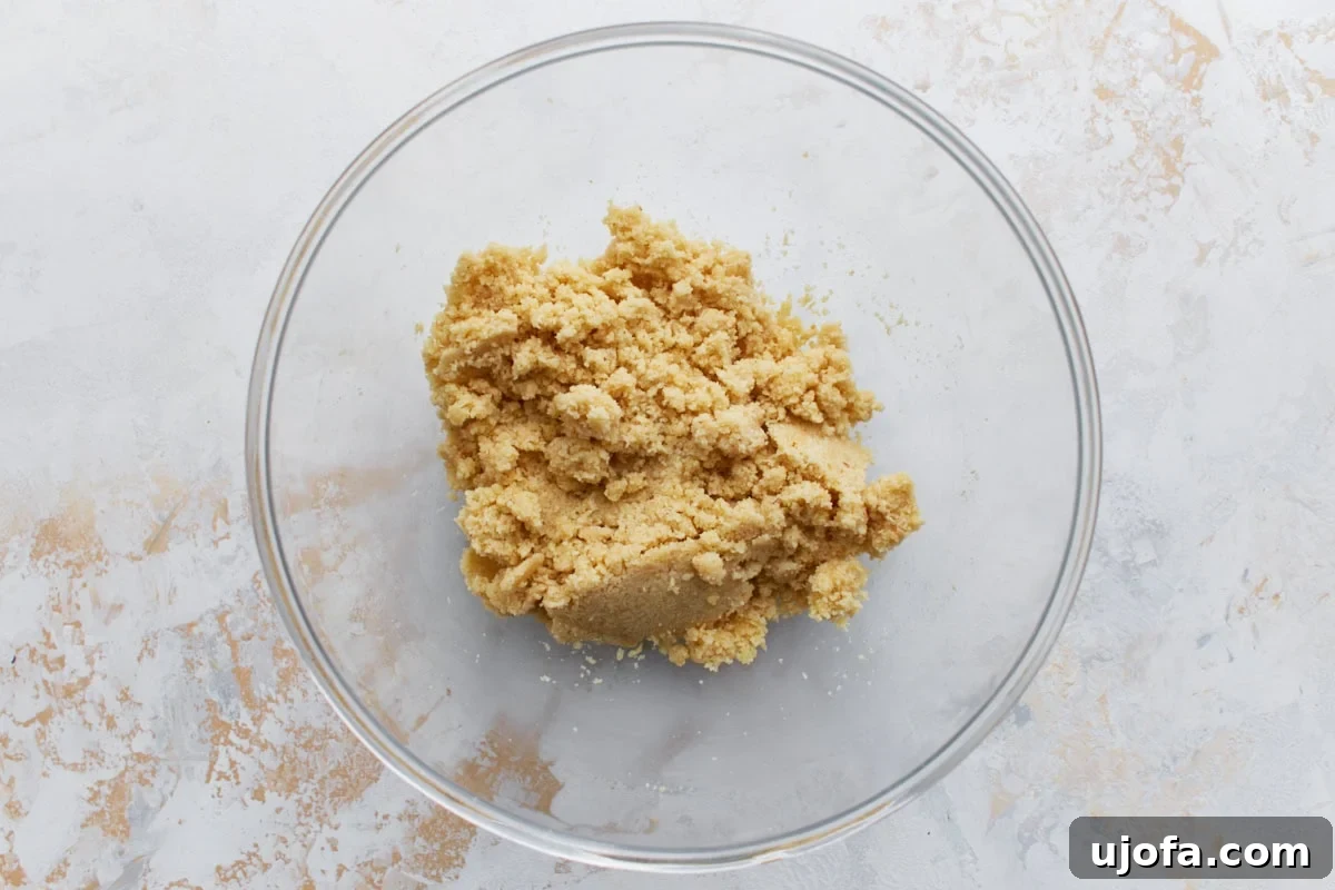 Decadent Keto Cheesecake 5 Crumbly almond flour crust dough mixture in a clear glass mixing bowl.