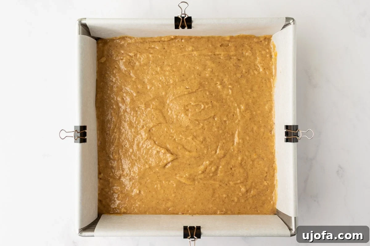 Spice cake batter spread evenly in a parchment-lined square baking pan, ready to bake.
