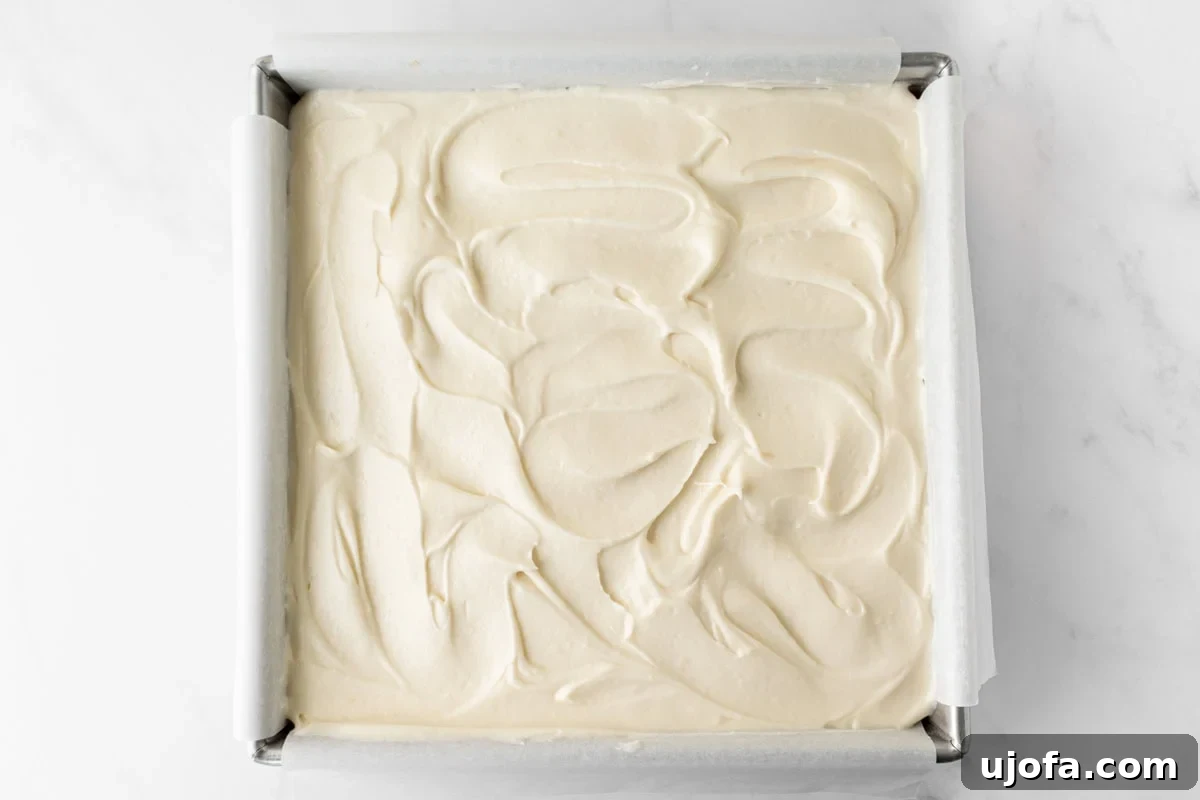 Gluten-free spice cake topped with swirled cream cheese frosting in a parchment-lined square pan.