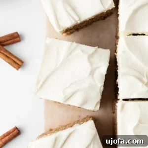 Top-down view of sliced gluten-free spice cake with cream cheese frosting on parchment paper, with cinnamon sticks nearby.