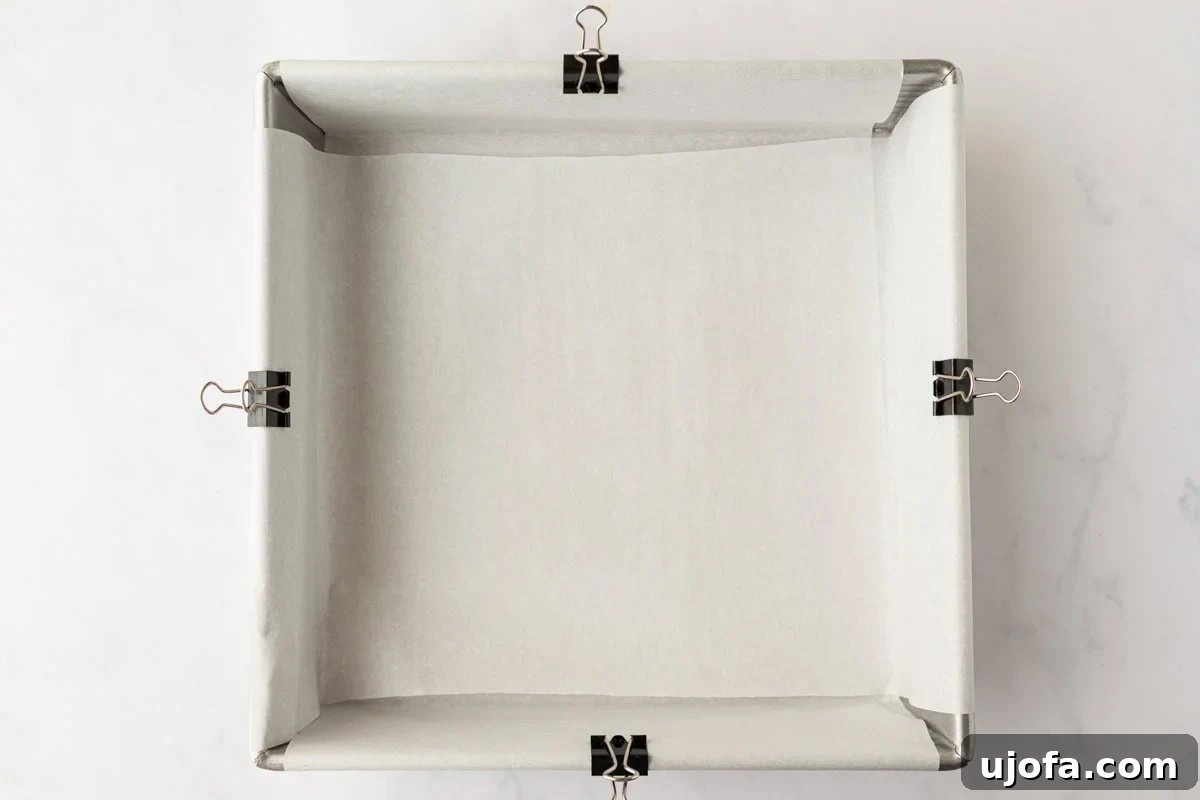 9x9-inch square baking pan lined with parchment paper and clipped at the edges for easy cake removal.