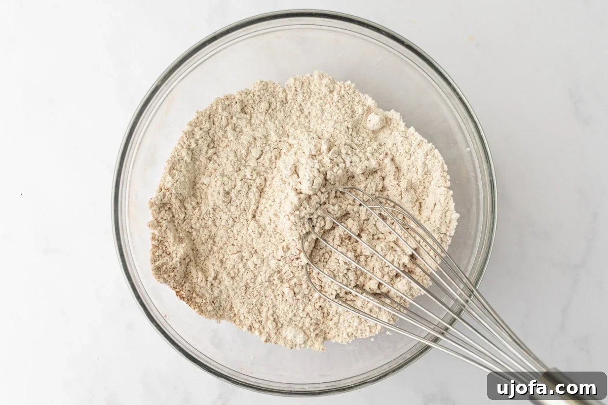 Glass mixing bowl with whisked gluten-free flour and warm spices like cinnamon, ginger, and nutmeg.