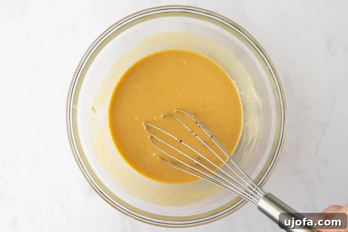 Smooth, pale orange batter in a glass bowl after combining eggs, sour cream, and applesauce.