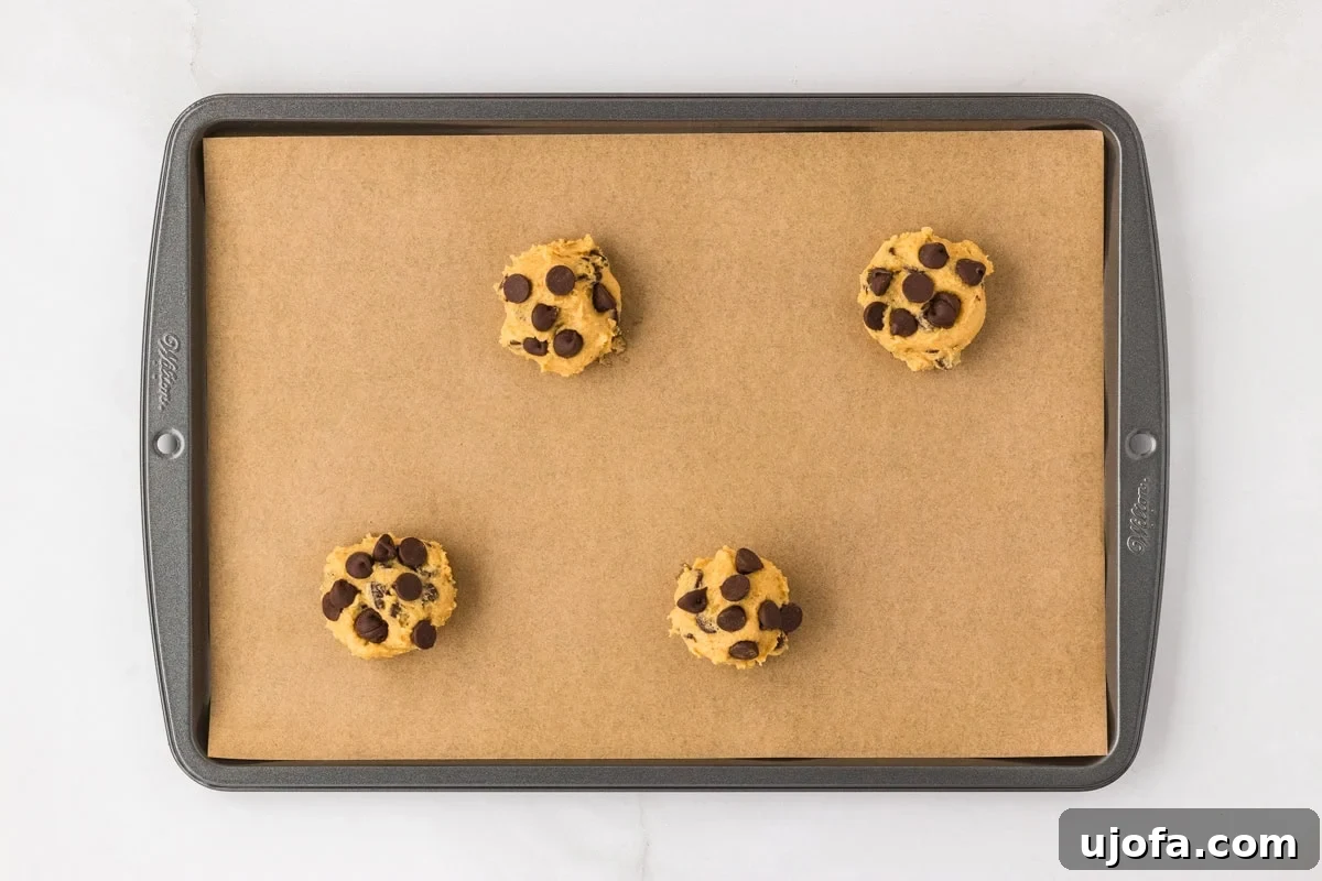 Four perfectly scooped balls of chickpea chocolate chip cookie dough placed on a parchment-lined baking sheet, spaced for even baking.