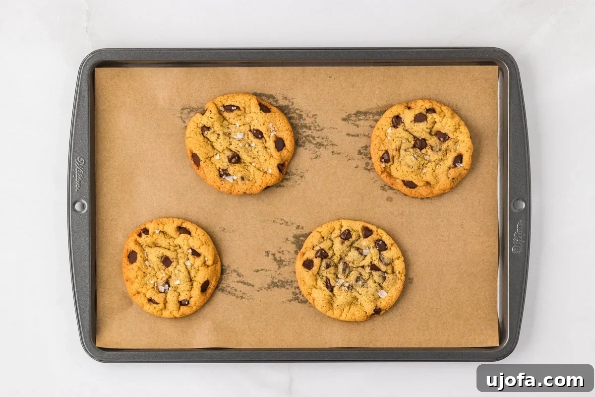 Four freshly baked chickpea chocolate chip cookies, golden brown at the edges, resting on a parchment-lined baking sheet.