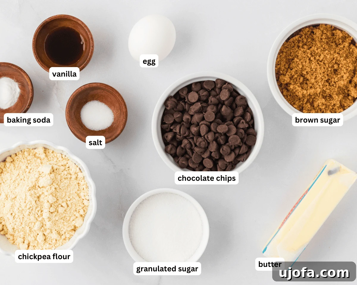 Collection of chickpea chocolate chip cookie ingredients laid out on a table: chickpea flour, butter, sugars, egg, vanilla, chocolate chips, baking soda, and salt.