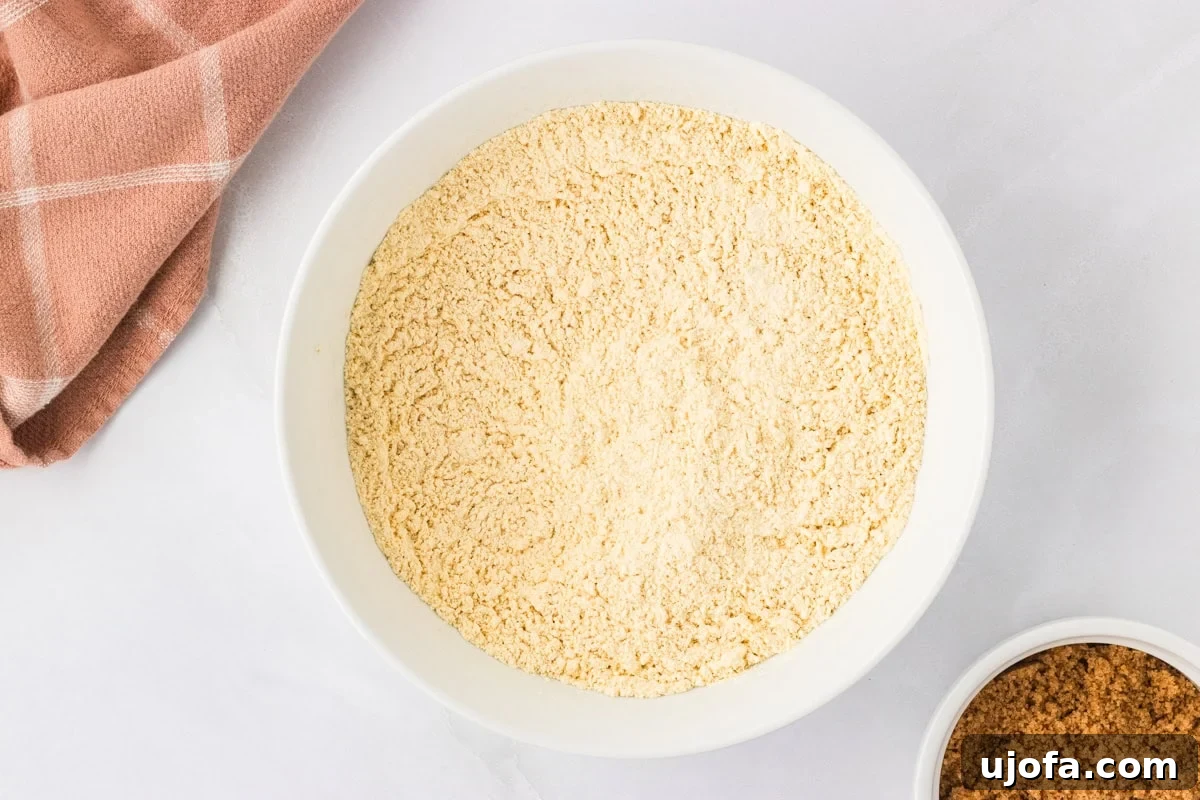 Bowl of chickpea flour on a white countertop with a brown napkin beside it, ready to be mixed with other dry ingredients.