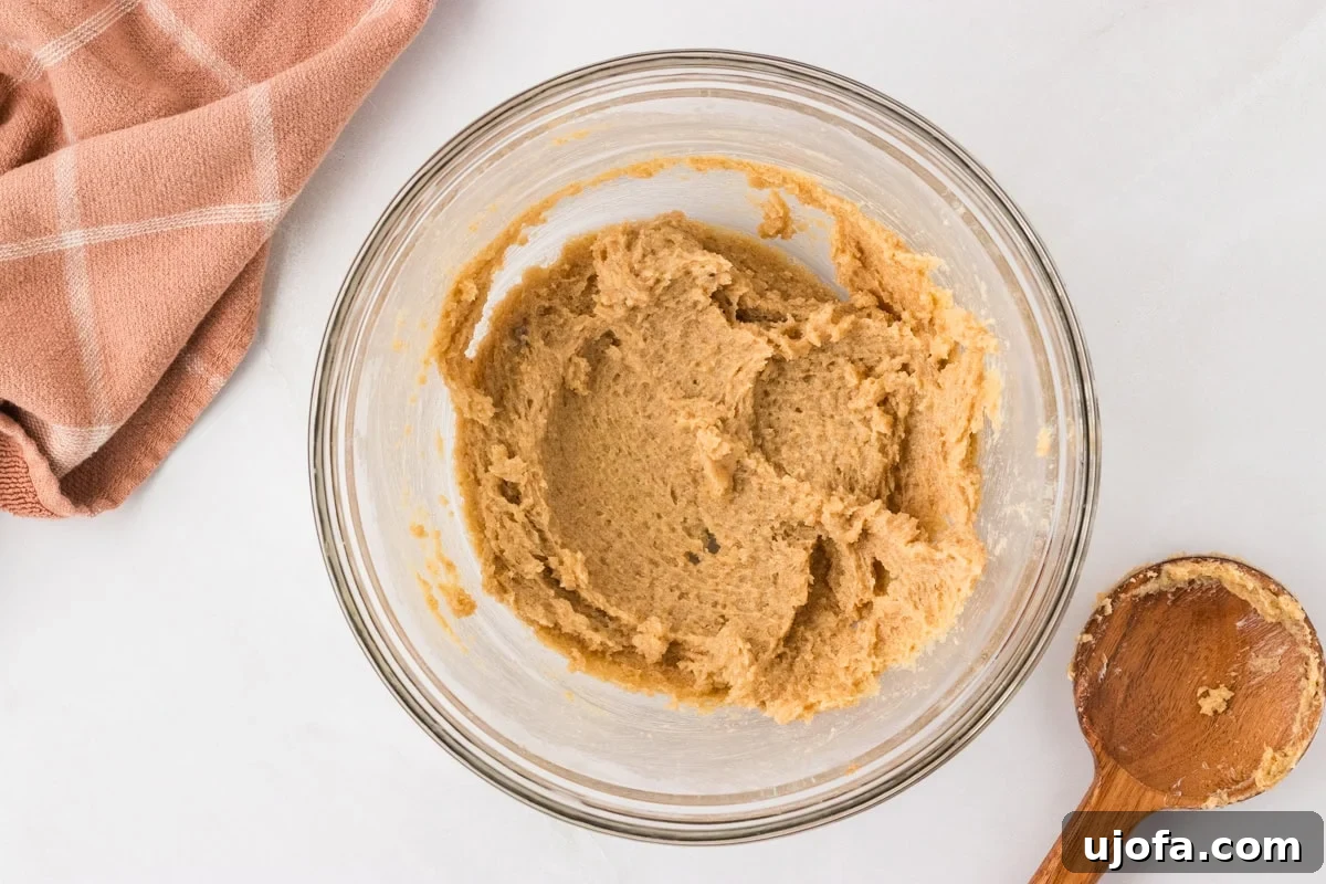 Creamed butter and sugar mixture in a glass mixing bowl with a wooden spoon, showcasing the light and fluffy texture.