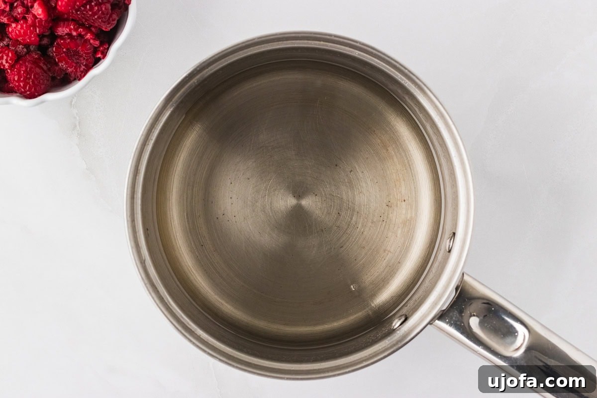 A silver saucepan with simple syrup being stirred over a burner.