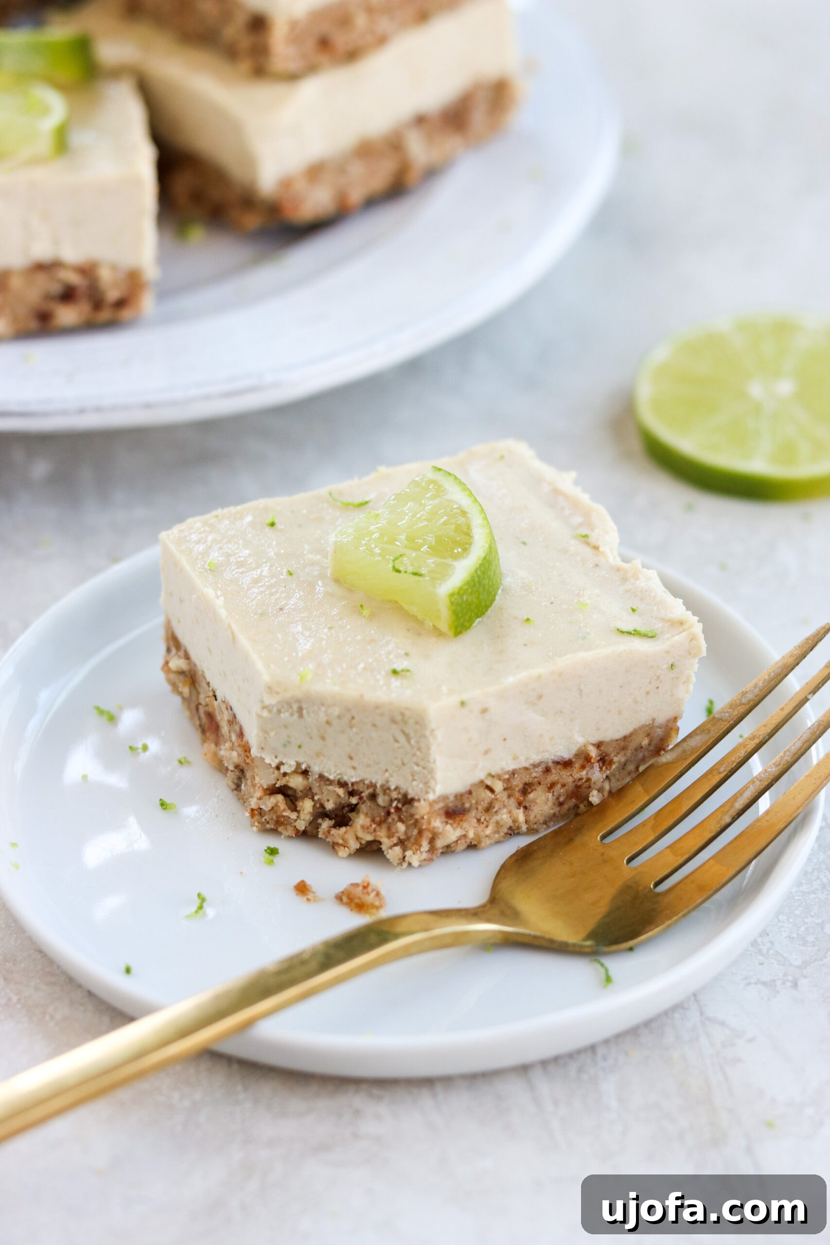 a vegan key lime cheesecake bar on a small white plate with a gold fork