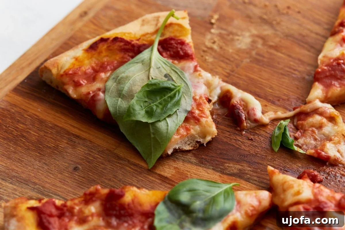 Plant-Based Pizza Perfection 13 a slice of vegan pizza topped with fresh basil, showing melted cheese and tomato sauce on a wooden board.