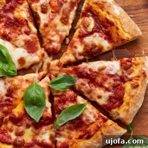 A baked vegan pizza sliced into wedges, topped with tomato sauce, melted vegan cheese, and fresh basil leaves on a wooden board.