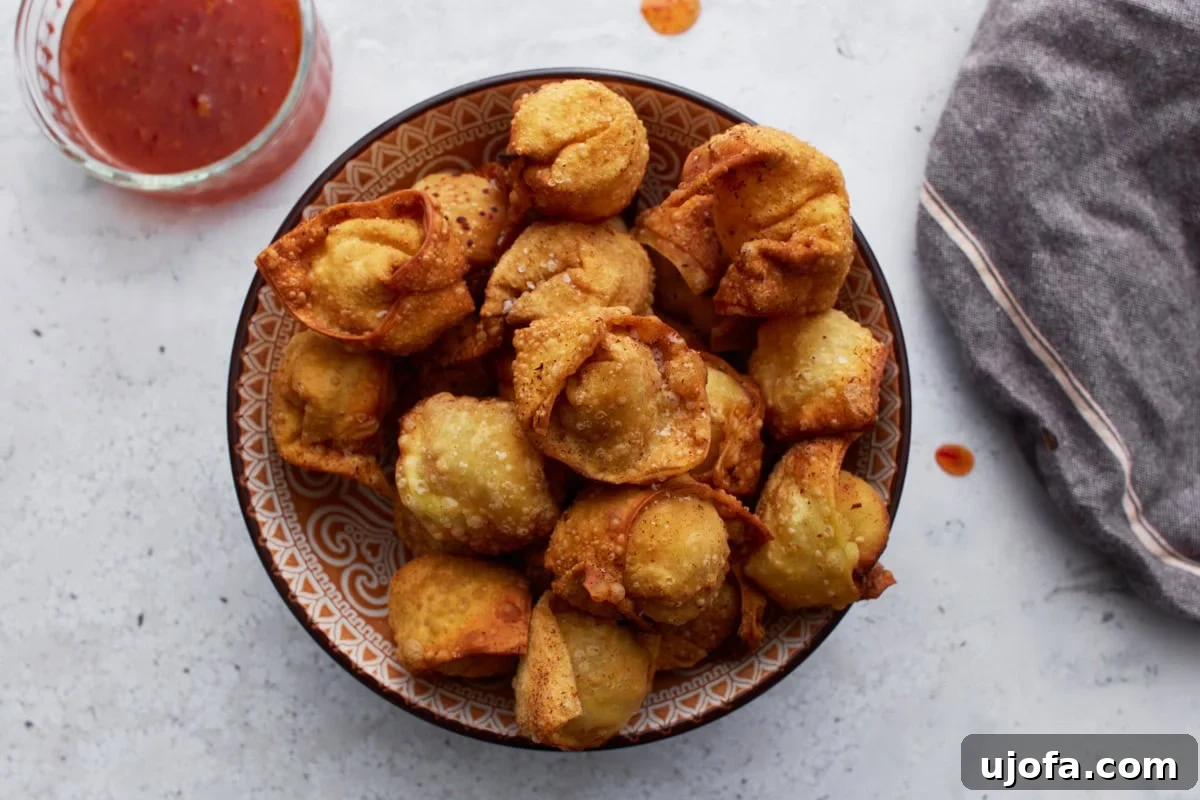 Gluten-free crab rangoons served in a bowl, with a small dish of sweet chili sauce nearby.