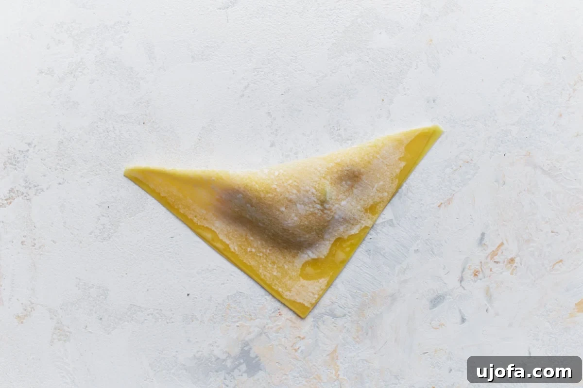 The edges of a wonton wrapper being moistened with water for sealing.