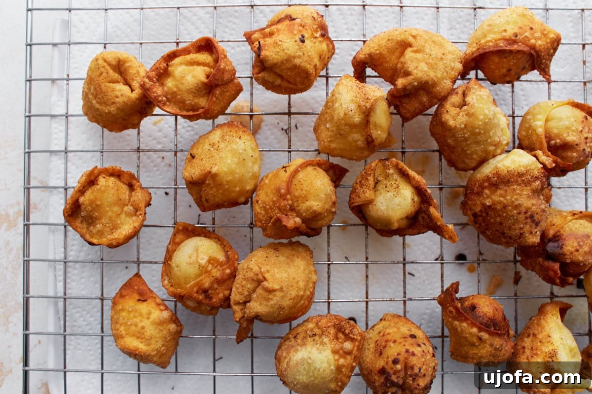 Freshly fried gluten-free crab rangoons draining on a wire rack.