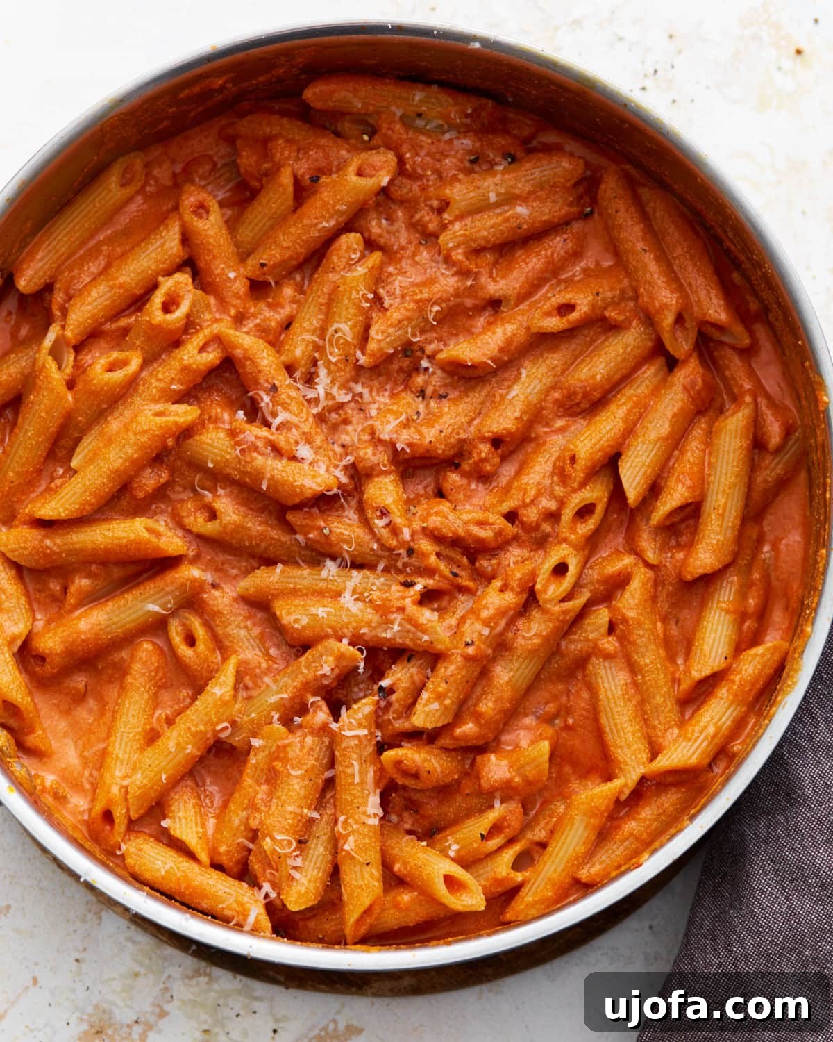 A pan filled with gluten-free penne pasta coated in creamy vegan vodka sauce, sprinkled lightly with vegan parmesan.